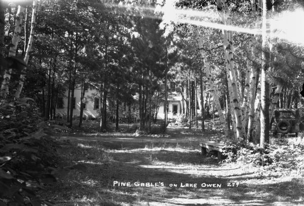 View looking down a dirt road. Two cabins and an automobile are visible through the trees at Pine Gable's on Lake Owen.