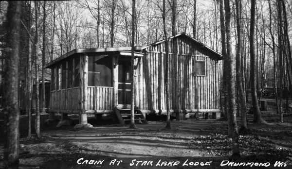 Exterior view of a log cabin at the Star Lake Lodge. There is a front porch on the left and trees surround the cabin.