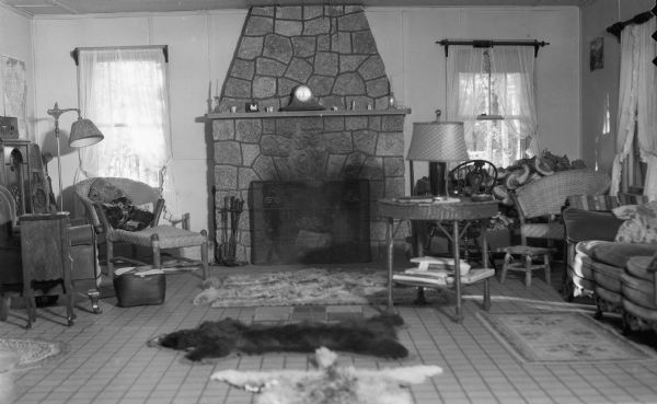 Interior view of a cabin with fireplace, bear rugs, tables, chairs and lamps.