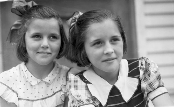 Close-up photograph of twin girls, both wearing dresses and with bows in their hair.