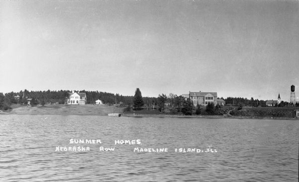 View from the lake of the summer homes on Nebraska Row along the shoreline of Lake Superior. The water tower and church steeple are visible on the far right.
