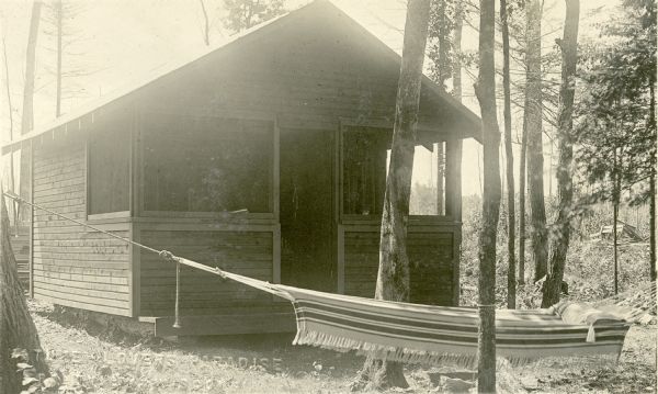 Exterior view of a small one-story wooden cottage with a front porch located on the land owned by Nature Lovers Paradise resort on Jackson Lake. The cottage is surrounded by small trees, and a hammock is in the foreground. Text describing this photograph says, "these are on our land but are not rented out."<p>Located within the Chequamegon National Forest, Jackson Lake is a 142-acre drainage lake with a navigable outlet channel to Namakagon Lake – which is a 3,227 acre drainage lake at the headwaters of the Namakagon River in Bayfield County, Wisconsin.</p>