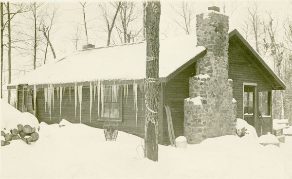 Exterior view of a one-story wood cottage or cabin with a stone chimney and icicles handing off the roof. The ground and roof are covered in snow, and a pair of snowshoes and skis are in the foreground. This building is on land at the Nature Lovers Paradise resort on Jackson Lake.<p>Located within the Chequamegon National Forest, Jackson Lake is a 142-acre drainage lake with a navigable outlet channel to Namakagon Lake – which is a 3,227 acre drainage lake at the headwaters of the Namakagon River in Bayfield County, Wisconsin.</p>