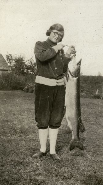 View of a woman standing outside holding a large fish that was caught at Nature Lovers Paradise, a resort on Jackson Lake. Located within the Chequamegon National Forest, Jackson Lake is a 142-acre drainage lake with a navigable outlet channel to Namakagon Lake – which is a 3,227 acre drainage lake at the headwaters of the Namakagon River in Bayfield County, Wisconsin.