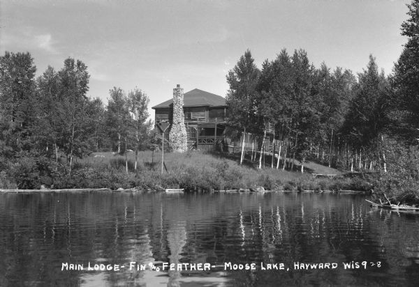 Lakeside view of large two-story log lodge with outside stone chimmney at Moose Lake.