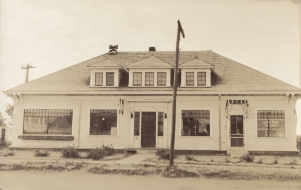 Exterior view of the front facade of a building. The left side has a sign that says: "State Bank of Drummond" and the window on the right says: "Soda and Ice Cream Shop."