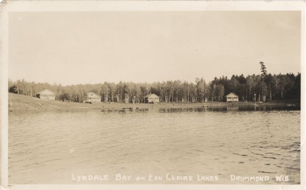 View across lake towards four single-story cabins with front porches along the shoreline of Lyndale Bay on Eau Claire Lakes.