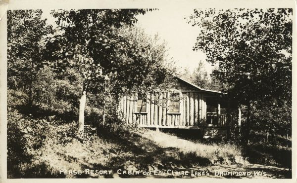 View of a single-story log cabin with front porch in the woods.