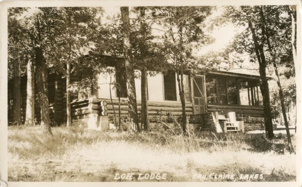 Exterior view of front steps and porch of a single-story log cabin surrounded by trees.