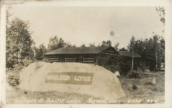 View of a large rock that says "Boulder Lodge." Behind the boulder are the cottages at Boulder Lodge.