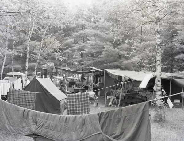 Elevated view of a family at "Midwaters Campground" at Hiawatha National Forest. The campsite is complete with tents, picnic tables, hanging blankets and towels.

