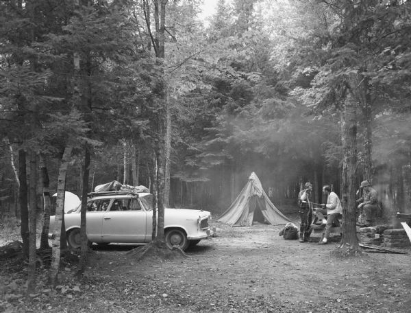 Three men holding archery equipment at a campsite in Hiawatha National Forest.