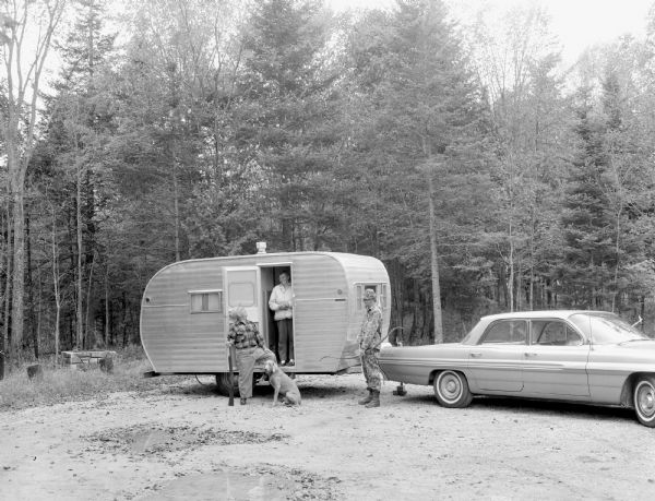 Two men, a woman, and a dog at a trailer in Hiawatha National Forest.