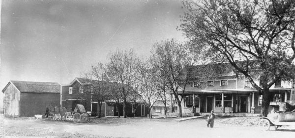 Copy photograph of a man and boy standing at the road. This location would later become the site of Jung's General Store. The photograph has a horse and buggy image pasted into the view on the left side.
