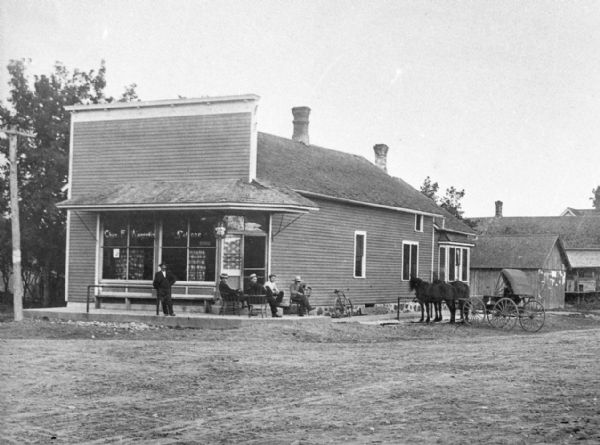 Copy photograph of the exterior of a saloon. A group of men lounge on the porch of the establishment.