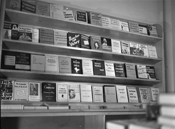 Interior of the People's Bookstore. Close-up of magazine and pamphlet shelves with many titles visible. Titles include "The History of the Communist Manifesto," "History of Anarchism in Russia," "The Negro in the Civil War," "Thomas Paine," "Women in the War" and "Public Speaking."