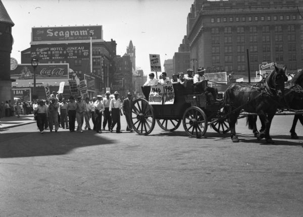 Part of a United Public Workers parade/demonstration on a downtown city street. A horse-drawn wagon carries some participants. Parade signs read "No Swivel Chair Politicians" "Elections are Coming. Hooray, Hooray" "1846 One-Horse Town, 1946 One Horse Pay!" Large brick and stone buildings rise in the background.