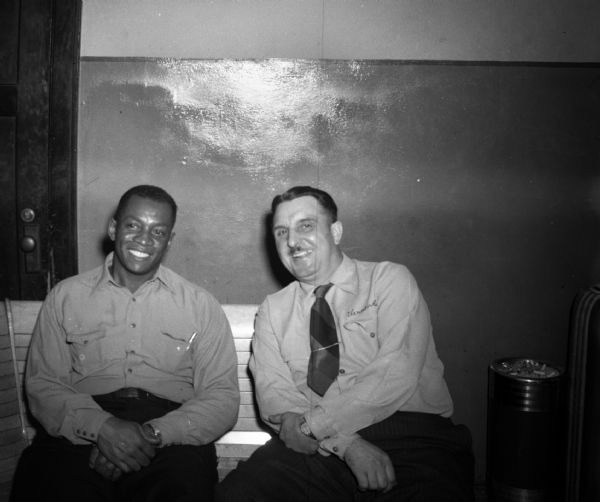 Nat Ferral and Vernon Brady, CIO bowling team captains, pose for a picture sitting on a bench at a bowling alley. Ferrel was captain of the all African American team from UAW local 575 (Sivyer Steel) and Brady was captain of a team from UAW local 407 (Unit Drop Forge).