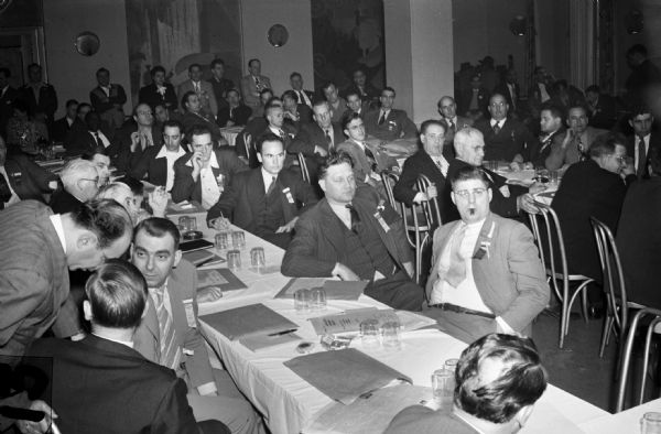 Conference room at the United Auto workers (UAW) farm implement conference. Attendees sit at banquet tables and stand along the walls in the crowded room.