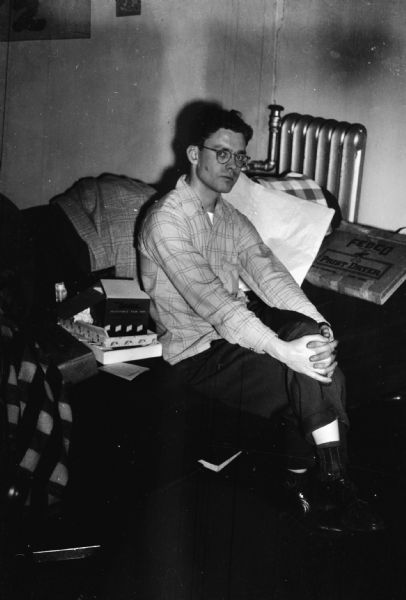 Portrait of Richard Brobst sitting on a couch. Opened packages of photography equipment are next to him.