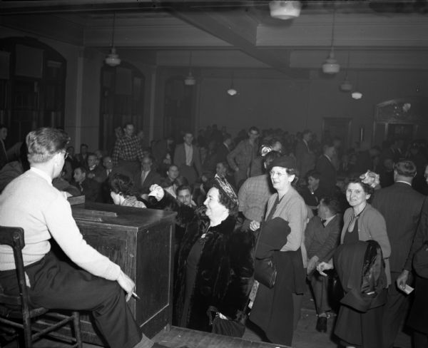Women casting ballots at the Lithographers' Local #7 Strike vote. The ballot box is on a stage at the front of a large crowded room.