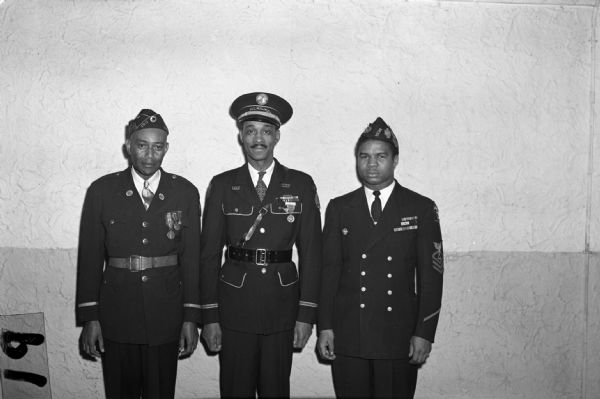 Memorial Day, "Poppy Day," Committee. Three men in uniform stand for a group portrait in front of a stucco wall.