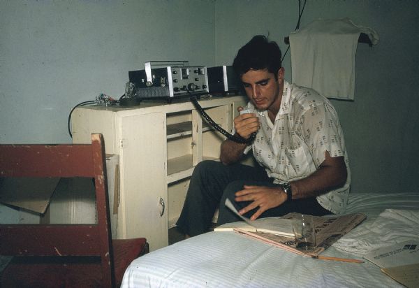 Member of the anti-Castro group Commandos L sitting on a bed testing a new radio transmitter-receiver.