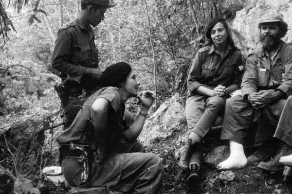 26th of July Movement soldiers, including Raúl Castro and Vilma Espin, resting by a rocky cliff-side in Oriente Province during the Cuban Revolution.