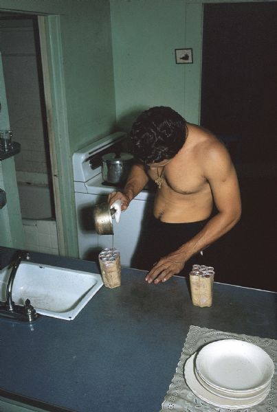 Member of the anti-Castro group Commandos L manufacturing explosives in a kitchen. The man is pouring a liquid from a small pot into a bundle of metal tubes.