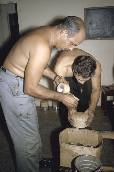 Two members of the anti-Castro group Commandos L working together to tape a homemade explosive device closed.
