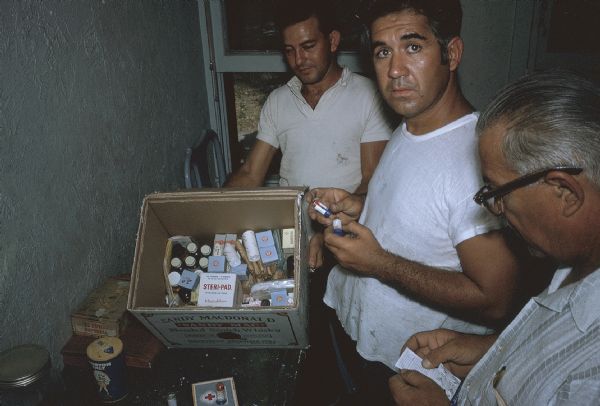 Three members of the anti-Castro group Commandos L with a cardboard whiskey box full of first aid supplies.