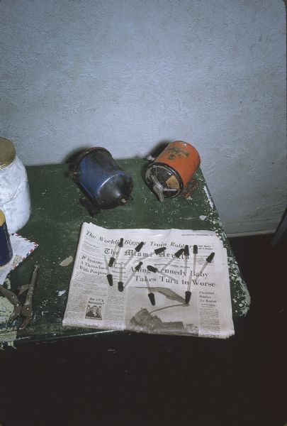 Close-up of a collection of eyedroppers on a newspaper and metal canisters at the barracks/armory of the anti-Castro group, Commandos L. Eyedroppers were probably used to manufacture explosives.