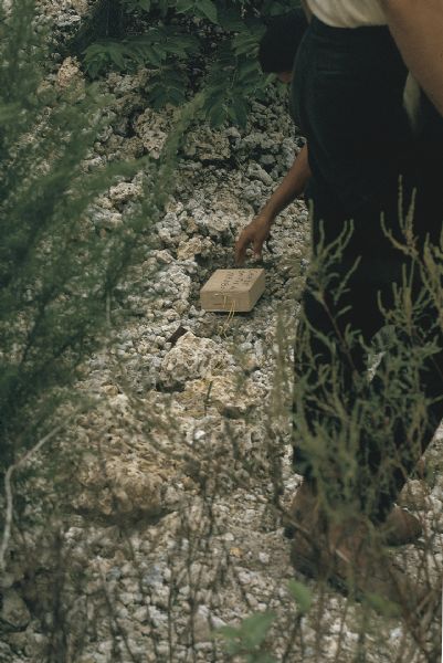 Close-up of a homemade incendiary device being tested by two men of the anti-Castro group Commandos L in the Everglades. The brown box has wires connected to it and is sitting on rocky ground.