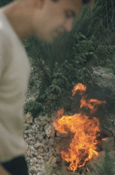 Fire set by an incendiary device made by the anti-Castro group Commandos L. In the extreme foreground the blurred image of a member of the group frames a small fire on the rocky ground in the Everglades.