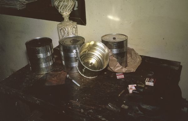 Close-up of cans used for homemade explosives by the anti-Castro group Commandos L. The cans are sitting on a table with a lamp, a bowl and books of matches.