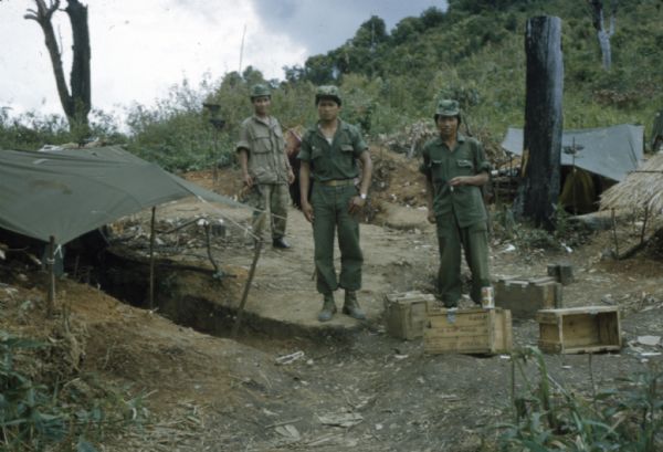Three Lao infantrymen stand outside near of tents in the Keukacham village.