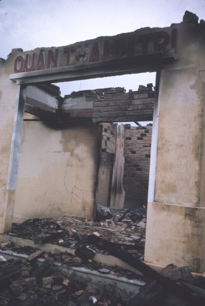 Entrance to a wrecked building destroyed by the Viet Cong in Vinh Quoi, Vietnam. The building is filled with brick debris and has a sign that reads, "Quàn Thanh Tri."