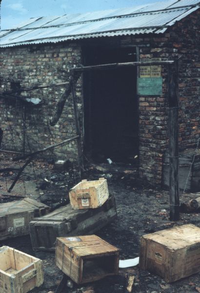 Alley in Vinh Quoi, Vietnam, after a Viet Cong attack. Empty wooden ammunition boxes are strewn about in front of the charred entryway to a small brick building.