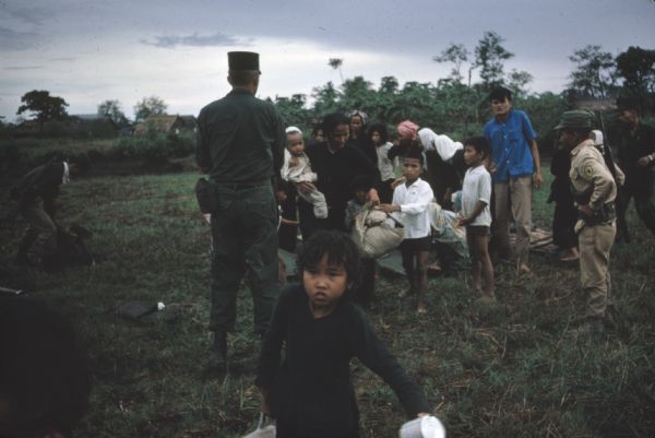 Soldiers stand in front of a group of survivors of a Viet Cong attack on the village of Vinh Quoi. The survivors are carrying bundles of belongings and a girl is walking past the photographer in the foreground.