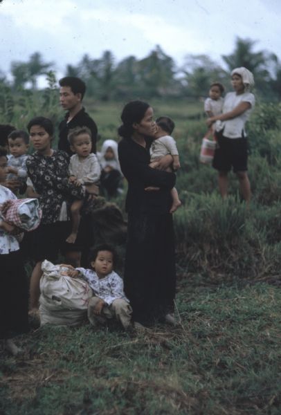 Survivors of a Viet Cong attack on the village of Vinh Quoi stand in a grassy field. The group is mostly women holding children and standing with belongings.