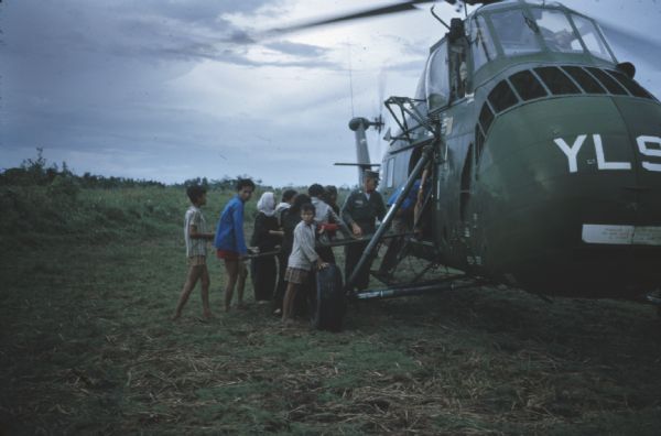 Group of villagers carry a stretcher holding a man injured during a Viet Cong attack on the village of Vinh Quoi into a US Marine helicopter for medical evacuation. A soldier stands next to the helicopter door.