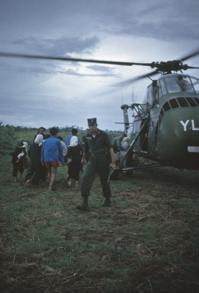 Survivors of a Viet Cong attack on the village of Vinh Quoi load onto a helicopter for medical evacuation. In the foreground a soldier carrying a rifle walks away from the helicopter.