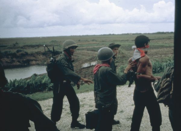 Vietnamese Rangers escort a newly captured prisoner suspected of being Viet Cong down a gravel road in the vicinity of Bac Lien, Vietnam. The prisoner has his elbows tied behind his back and is blindfolded.