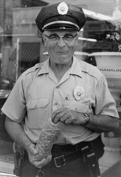 Wautoma Police Chief, Max Blader, in uniform, smiles while he eats grapes during a grape boycott picket.
<p></p>El Jefe de Policía de Wautoma come uvas durante el boicot
<p></p>El Jefe de Policía, Max Blader, vestido en uniforme, sonríe mientras come uvas durante un piquete del boicot de uvas.