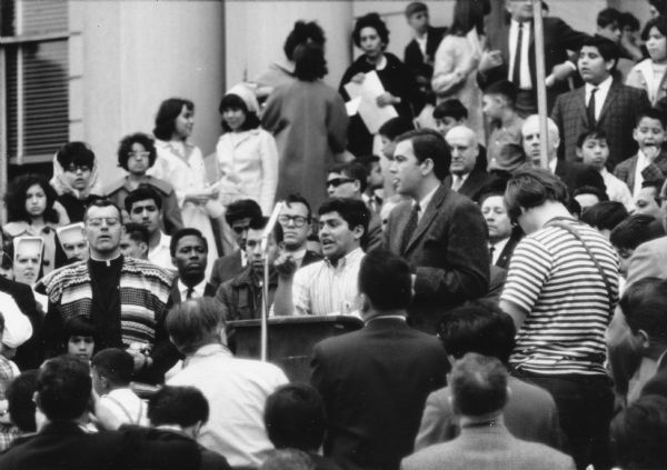 Wisconsin agricultural labor union Oberos Unidos founder Jesús Salas addressing a rally crowd from a podium after a farm worker demonstration. The crowd is both grouped behind him on steps and standing in front of him.<p>Obreros Unidos translates to "United Workers." According to David Giffey and Jesús Salas, Obreros Unidos was a migrant farm-worker labor union which grew in Wisconsin during the 1960s, deeply rooted in Mexico and South Texas. The union was created by workers to address discriminatory, oppressive living and working conditions in Wisconsin and elsewhere in in the northern parts of the United States. Salas, a third-generation farm worker whose family relocated to Wautoma in 1958, became the union's leader.

<p></p>Jesús Salas se dirige al público durante una protesta<p></p>Jesús Salas, fundador de Obreros Unidos, un sindicato para trabajadores agrícolas en Wisconsin, se dirige al público desde un podio después de una demonstración de trabajadores agrícolas. La gente está agrupada detrás de él en unos escalones y parados enfrente de él.

<p></p>
Obreros Unidos se traduce a "United Workers" en inglés. De acuerdo a David Giffey y Jesús Salas, Obreros Unidos fue un sindicato de trabajadores agrícolas emigrantes que se desarrollo en Wisconsin durante los años 1960, y con raíces profundas en México y el sur de Texas. El sindicato fue formado por trabajadores para combatir las prácticas discriminatorias, las condiciones opresivas de vivienda y de trabajo en Wisconsin y en otros lugares en las partes del norte de los Estados Unidos. Salas, parte de una tercera generación de trabajadores agrícolas, cuya familia se mudo a Wautoma en 1958, se volvió el líder del sindicato.
