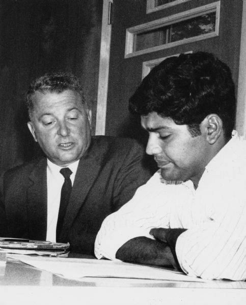 On the right, Jesus Salas, leader of Obreros Unidos (United Workers), Wisconsin's migrant farm worker union. On the left, John Schmitt, president of the AFL-CIO. They are sitting in a meeting.<p>Strikes in Wisconsin were organized by the Obreros Unidos, an independent farm worker labor union effort in the 1960s.<p>Jesus Salas y John Schmitt<p>A la derecha, Jesús Salas, líder de Obreros Unidos, un sindicato para trabajadores emigrantes en Wisconsin. A la izquierda, John Schmitt, presidente de la AFL-CIO. Están sentados durante una audiencia. Las huelgas en Wisconsin fueron organizadas por Obreros Unidos, un esfuerzo independiente del sindicato de trabajadores agrícolas durante los años 1960.</p>