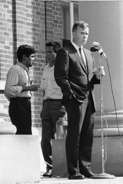 Reverend Barry Shaw, of the Wisconsin Council of Churches, speaks at the microphone addressing a rally in Wautoma. Behind him are Jesus Salas and Salvador Sanchez, leaders of the National Farm Workers' Association march in Wisconsin.<p>This photograph is a part of Wisconsin-native David Giffey's series "Struggle for Justice," images from the migrant farm worker struggle including an independent oganizing effort in Wisconsin and the nationwide grape boycott movement started by Cesar Chavez of United Farm Workers during the 1960s and 1970s.<p>El Reverendo Barry Shaw<p>El Reverendo Barry Shaw del consejo de iglesias o Wisconsin Council of Churches usa un micrófono para hablarle a la manifestación en Wautoma. Detrás de él están Jesús Salas y Salvador Sánchez, líderes de la marcha de National Farm Workers' Association en Wisconsin. Esta fotografía es parte de la serie "Lucha por la Justicia" tomada por David Giffey, originario de Wisconsin, las imágenes muestran la lucha de los trabajadores agrícolas emigrantes incluyendo un esfuerzo independiente organizado en Wisconsin y el movimiento nacional del boicot de uvas empezado por Cesar Chávez de la unión de campesinos o United Farm Workers durante los años 1960 y 1970.</p>