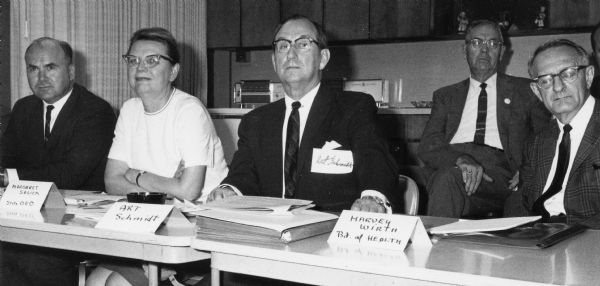 A panel of Wisconsin state officials at Waushara County Electric Cooperative building meeting with Oberos Unidos (United Workers) migrant farm workers union members (off camera). The meeting was held in the evening where union leaders were asking that demands for $1.25 minimum wage, insurance benefits, meeting with the Governor's committee and public sanitation facilities for migrant farm workers be met.<p>After the meeting, Jesus Salas announces, "We will continue to march" to Madison to make demands and meet with officials at the Capitol.<p>Strikes, rallies and marches in Wisconsin were organized by Obreros Unidos (United Workers), an independent labor union founded in Central Wisconsin to improve conditions for migrant farm workers in the 1960s.<p>Panel estatal en el edificio de Waushara County Electric Cooperative<p>Un panel de oficiales del estado de Wisconsin en el edificio de Waushara County Electric Cooperative en una junta con trabajadores agrícolas emigrantes miembros de Obreros Unidos (fuera de cámara). La junta fue mantenida en la tarde, en la cual los líderes de sindicato pidieron que las demandas por un sueldo mínimo de $1.25 por hora, beneficios de aseguranza, una junta con el comité del gobernador, e instalaciones sanitarias públicas para los trabajadores agrícolas emigrantes fueran cumplidas. Después de la junta, Jesús Salas anuncio, "Continuaremos la marcha" hacia Madison para hacer demandas y tener reuniones con oficiales en el Capitolio. Las huelgas, manifestaciones, y marchas en Wisconsin fueron organizadas por Obreros Unidos, un sindicato independiente fundado en el centro de Wisconsin para mejorar las condiciones de los trabajadores agrícolas emigrantes durante los años 1960.</p>