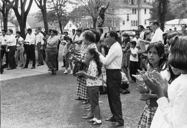 A group of National Farm Workers Association members and supporters applauding rally speakers in front of Waushara County Courthouse. A march to the rally was led by Jesus Salas, Obreros Unidos (United Workers) leader where he and others spoke about making demands for better working conditions for Wisconsin migrant farm workers to state officials.<p>Strikes, rallies and marches in Wisconsin were organized by the Obreros Unidos, an independent farm worker labor union effort in the 1960s.<p>Simpatizantes del sindicato aplauden durante la manifestación en Waushara<p>Un grupo de miembros y simpatizantes de National Farm Workers Association aplauden los oradores de la manifestación enfrente del tribunal o Waushara County Courthouse. Una marcha de manifestantes fue guiada por Jesús Salas, líder de Obreros Unidos, donde él y otros hablaron de exigirles a los legisladores estatales mejores condiciones laborales para los trabajadores agrícolas emigrantes en Wisconsin. Las huelgas, manifestaciones, y marchas en Wisconsin fueron organizadas por Obreros Unidos, un esfuerzo independiente del sindicato de trabajadores agrícolas durante los años 1960.</p>