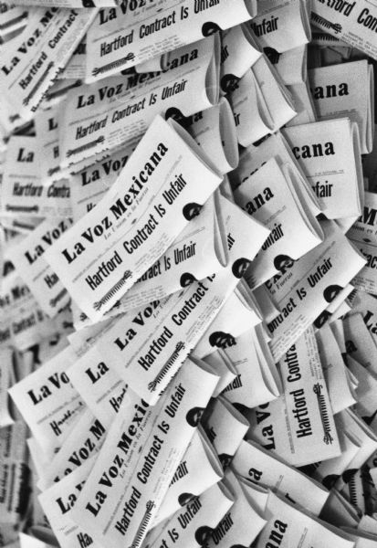 Piles of "La Voz Mexicana" (The Mexican Voice) newspapers at the Wautoma office of Obreros Unidos (United Workers). The headline says, "Hartford Contract is Unfair," referring to the cannery workers union contract with Libby's Hartford plant. Obreros Unidos called it unfair because the negotiations occur during winter.<p>This photograph is a part of Wisconsin-native David Giffey's series "Struggle for Justice," images from the migrant farm worker struggle including an independent organizing effort in Wisconsin and the nationwide grape boycott movement started by Cesar Chavez of United Farm Workers during the 1960s and 1970s.<p>Títulos de La Voz<p>Montones del periódico "La Voz Mexicana" en la oficina de Obreros Unidos en Wautoma. El titulo dice "El Contrato en Hartford es Injusto" ("Hartford Contract is Unfair"), refiriéndose al contrato sindical de los trabajadores especializados en enlatar con la planta de Libby en Hartford. Obreros Unidos lo llamó injusto porque las negociaciones ocurrieron en el invierno. Esta fotografía es parte de la serie "Lucha por la Justicia" tomada por David Giffey, originario de Wisconsin, las imágenes muestran la lucha de los trabajadores agrícolas emigrantes incluyendo un esfuerzo independiente organizado en Wisconsin y el movimiento nacional del boicot de uvas empezado por Cesar Chávez de la unión de campesinos o United Farm Workers durante los años 1960 y 1970.</p>